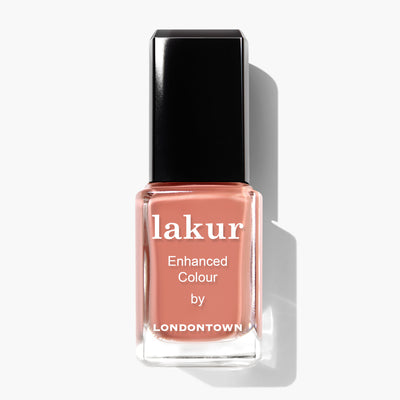 A bottle of LONDONTOWN's Pressed Petals enhanced color nail polish in a terracotta pink shade, featuring a subtle undertone of muted peach, with a black cap and a white background.