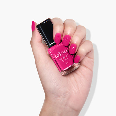A hand holding a bottle of LONDONTOWN's Queen of Hearts (Professional) nail polish in a deep fuchsia pink crème, with nails painted in the same vibrant color—perfect for a cruelty-free party manicure.