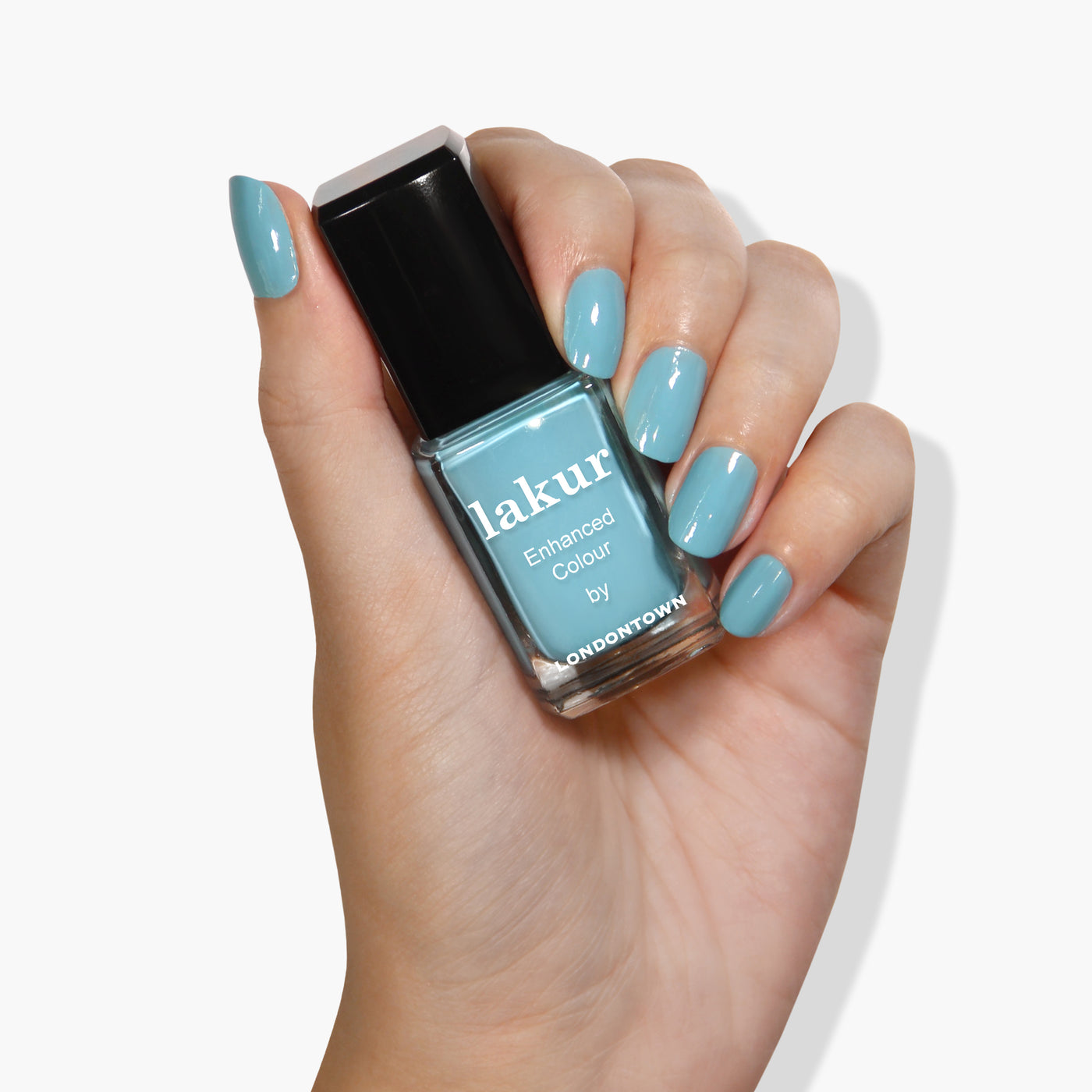 A hand with teal-colored painted nails is holding a bottle of LONDONTOWN's Lakur vegan nail polish in the shade Reverse the Charges.