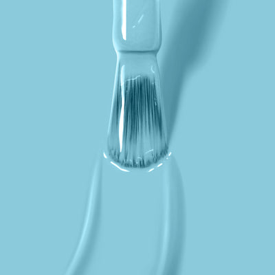 Close-up of a narrow paintbrush with light blue paint on its bristles against a matching blue background, reminiscent of LONDONTOWN's "Reverse the Charges (Professional)" serene aqua and turquoise nail polish collection.