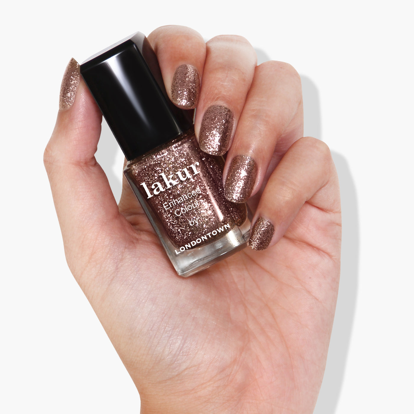 A hand holding a bottle of LONDONTOWN's Rosé All Day pink glitter nail polish polishes.