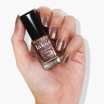 A hand holding a bottle of LONDONTOWN's Rosé All Day pink glitter nail polish polishes.