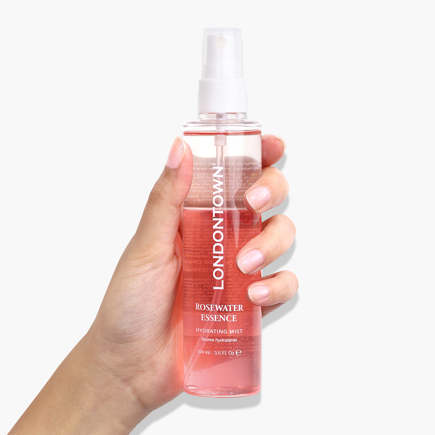 A hand holding a clear spray bottle labeled "LONDONTOWN Rosewater Essence Facial Mist," with rose-infused pink liquid inside.