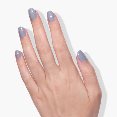 A hand with manicured nails painted in the glossy grayish-blue shade of LONDONTOWN’s Silver Birch nail polish is shown against a white background, highlighting the elegance of vegan and cruelty-free beauty.