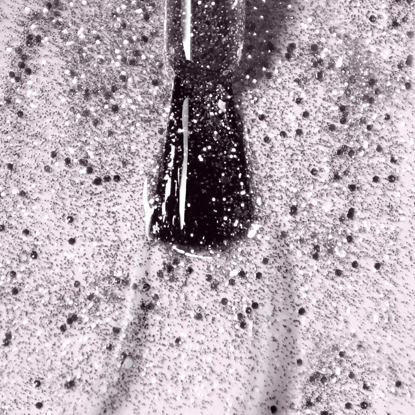 A close-up image of a nail polish brush applying LONDONTOWN's Starstruck (Professional), a vegan, cruelty-free silver glitter nail polish, on a surface. The shimmer polish’s glitter particles are scattered across the thin layer of polish.