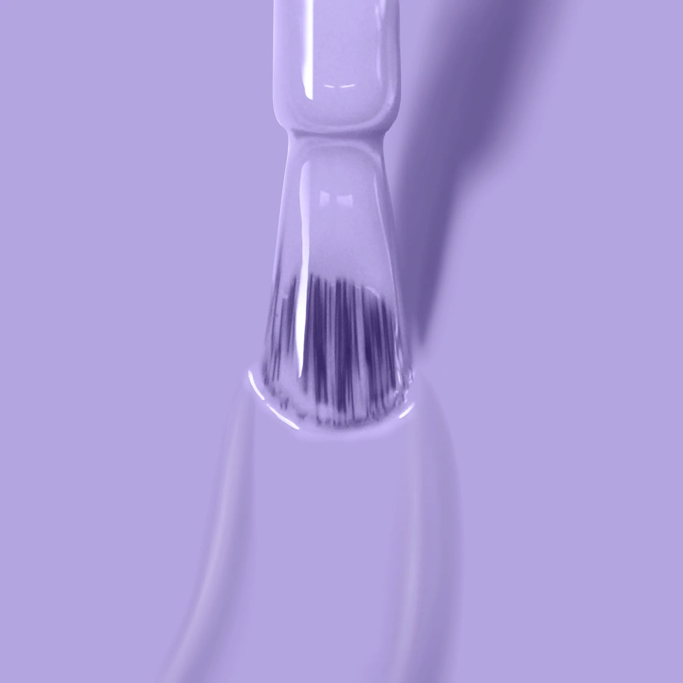 Close-up of a LONDONTOWN Trolley Away (Professional) nail polish brush applying lilac crème on a smooth surface, creating a glossy, even coat. The background is also light purple, providing a monochromatic aesthetic. This cruelty-free formula enhances beauty in an ethical way.