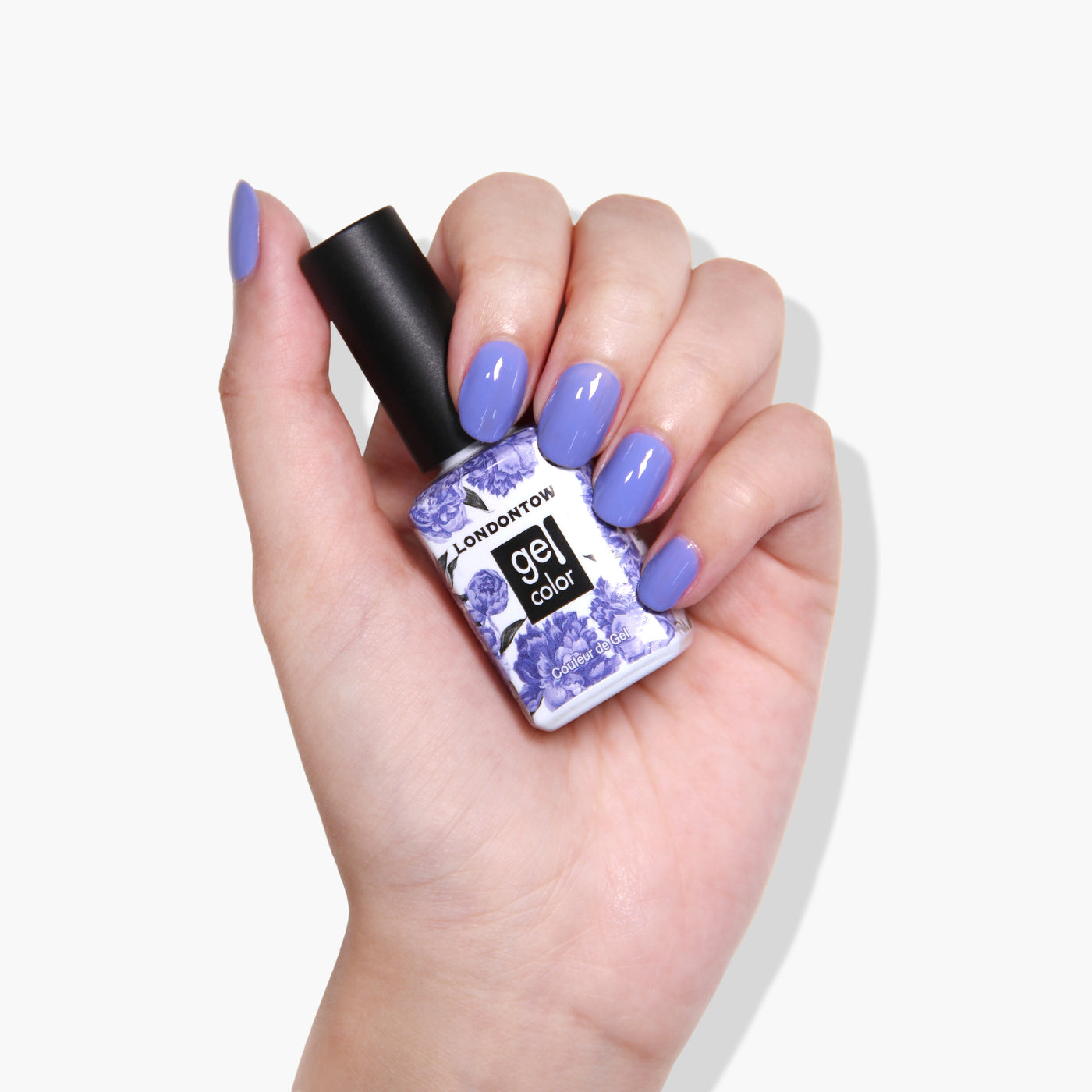 A hand holding a bottle of LONDONTOWN Uptown UV/LED Gel Color nail polish with nails painted in a bold lavender shade.
