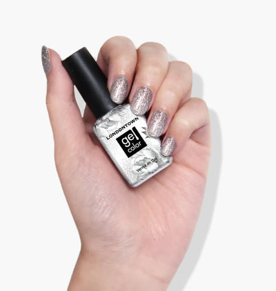 A hand with glittery silver nail polish holds a bottle of LONDONTOWN's Tiara, featuring a self-leveling formula for flawless wear, against a white background.