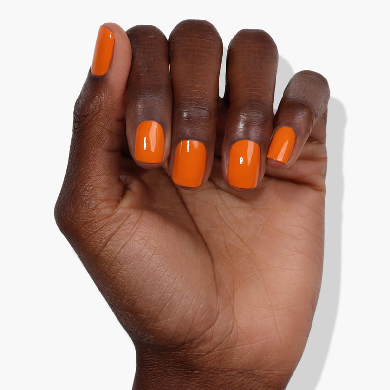 A hand with a dark skin tone is shown with nails painted in LONDONTOWN's vibrant burnt orange nail polish, Heat Wave, on a white background.