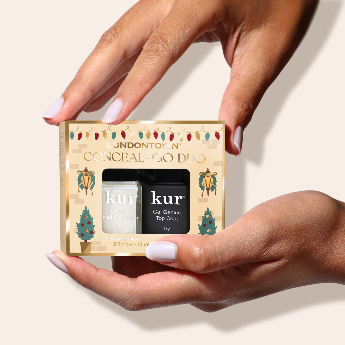 Two hands hold a LONDONTOWN Conceal & Go: Holiday Edition box containing white and black nail polish bottles—your essentials for perfect nails—set against a neutral background.
