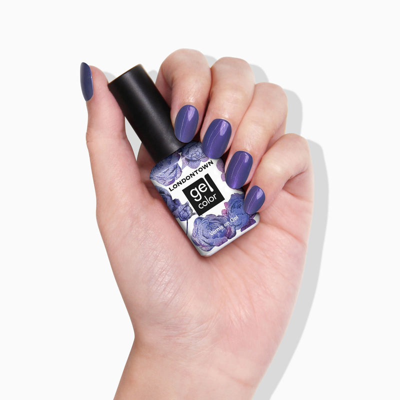 A hand with neatly manicured purple nails holds a LONDONTOWN Wildberry Freeze gel polish bottle with a floral label design and a subtle blue shimmer shift.