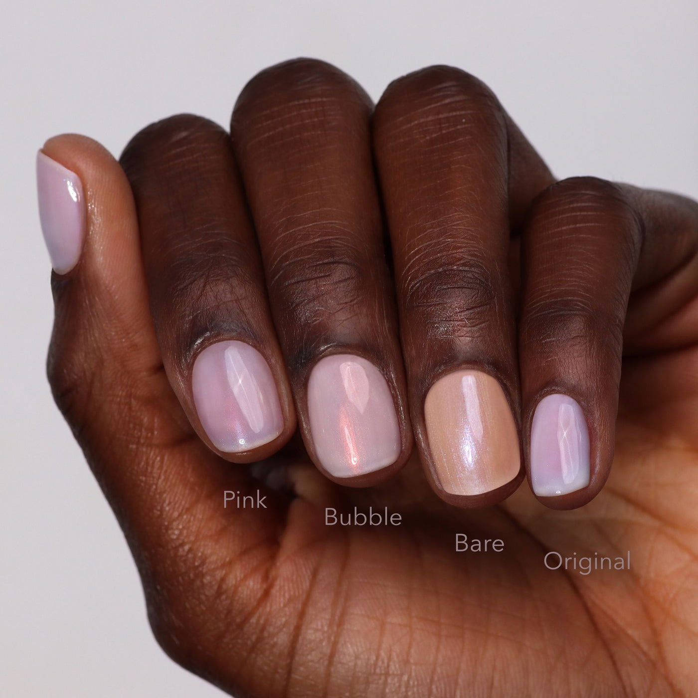 A hand with four fingernails painted in different nude shades from LONDONTOWN’s The Concealer Wardrobe is shown on a dark skin tone, highlighting easy care and beautiful nails.