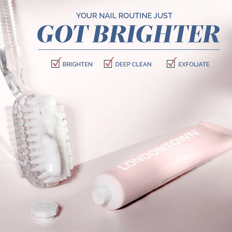Mani Bright Nail Scrub by LONDONTOWN sits on a light surface with its open tube, white cream, and brush. Text highlights its benefits: brighten, deep clean, and exfoliate—perfect for discolored or stained nails.