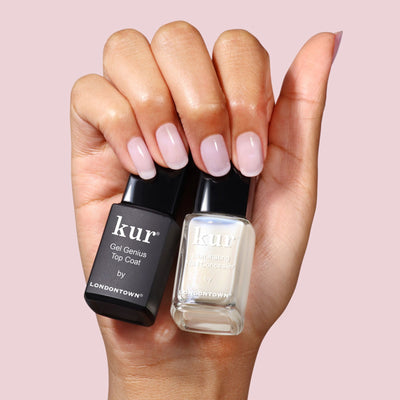 A hand with manicured, natural nails holds two LONDONTOWN bottles: the Conceal & Go: Holiday Edition and a top coat, for perfect nails.