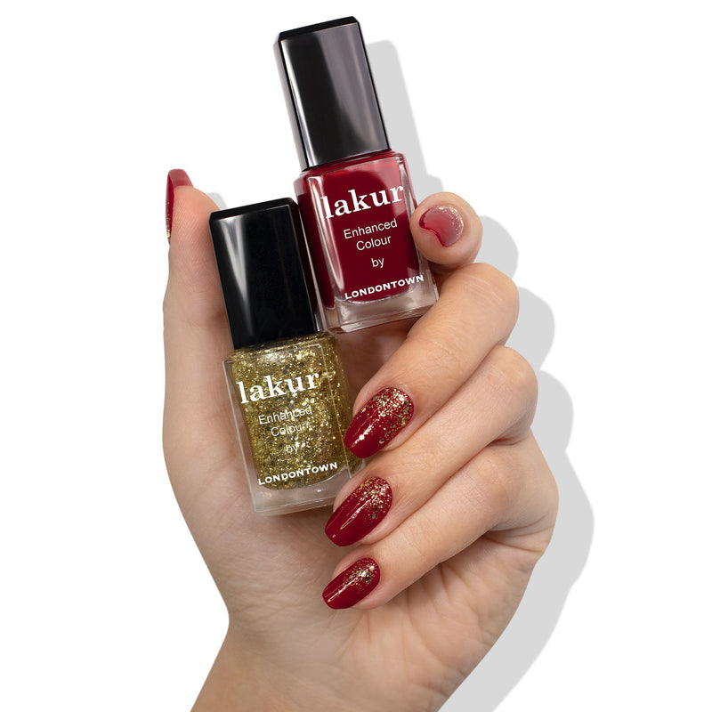 A hand with manicured nails painted red and gold glitter holds two LONDONTOWN Merry & Bright Duo nail polish bottles—one red, one gold—against a white background.