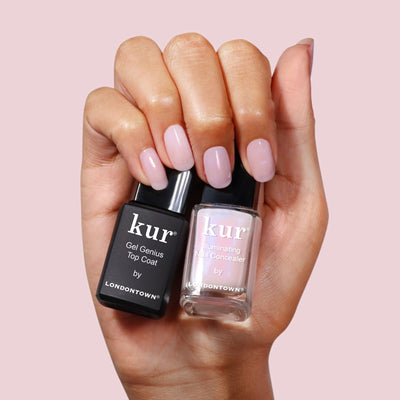 A hand with light pink polished nails holds LONDONTOWN’s Conceal & Go - Pink: Holiday Edition, highlighting this nail care essential against a pale pink background.