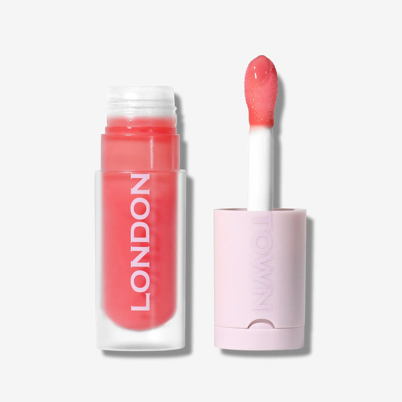 A tube of LONDONTOWN Quench Glow Buttery Lip Oil in Flushed, shown open with the applicator next to it and "LONDON" on the side, against a white background, offering hydrating shine and luscious pink color.