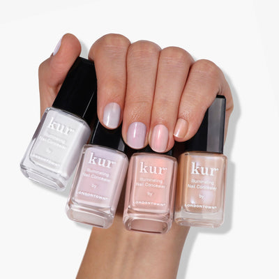 A hand holding four bottles of LONDONTOWN The Concealer Wardrobe, each in a different shade, with matching colors applied to the fingernails for effortless, one-step nail care.