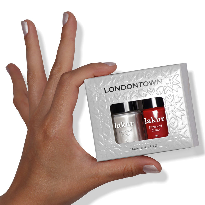 A hand holding a LONDONTOWN Frosted Berries Duo nail polish set, featuring two bottles, one white and one red, ideal for creating festive nails in its elegant rectangular packaging.