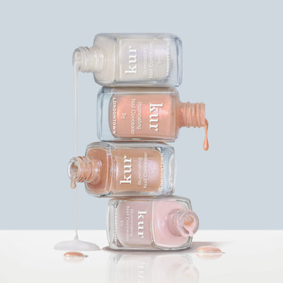 Four bottles of LONDONTOWN’s The Concealer Wardrobe nail polish are stacked and tilted, with the polish spilling and dripping onto a white surface below.