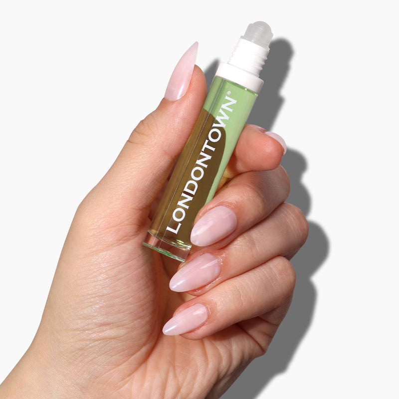 Hand holding a transparent, pocket-sized cylindrical container labeled "LONDONTOWN," filled with green liquid and featuring a rollerball applicator. This Roll & Glow Cuticle Oil - Agave Pear promises to be the sweetest addition to your nail care routine.
