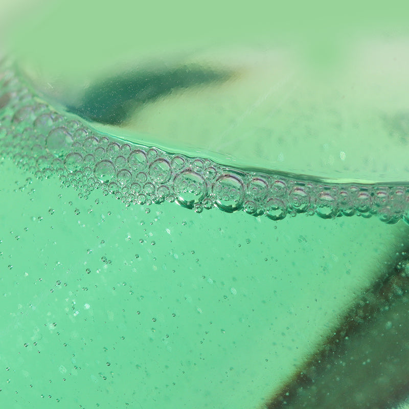 Close-up image of pocket-sized Roll & Glow Cuticle Oil - Agave Pear by LONDONTOWN, with bubbles forming along the surface, set against a blurred background.