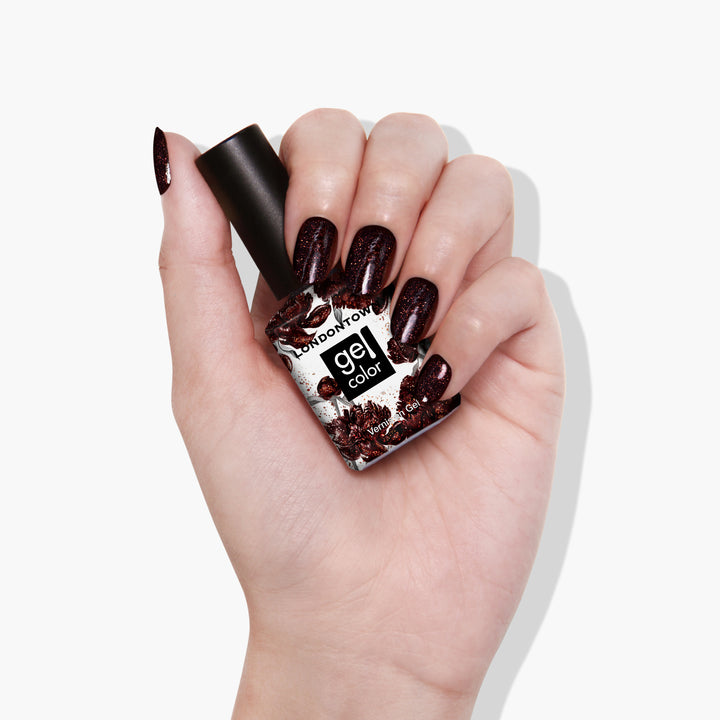 A hand with dark, glittery painted nails holds a bottle of LONDONTOWN&