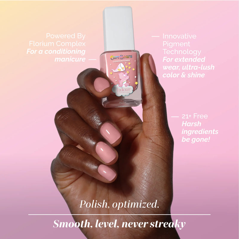 A hand with neatly manicured warm pink nails holds a bottle of LONDONTOWN BFF Care Bears-themed nail polish, with product benefits displayed around the image.