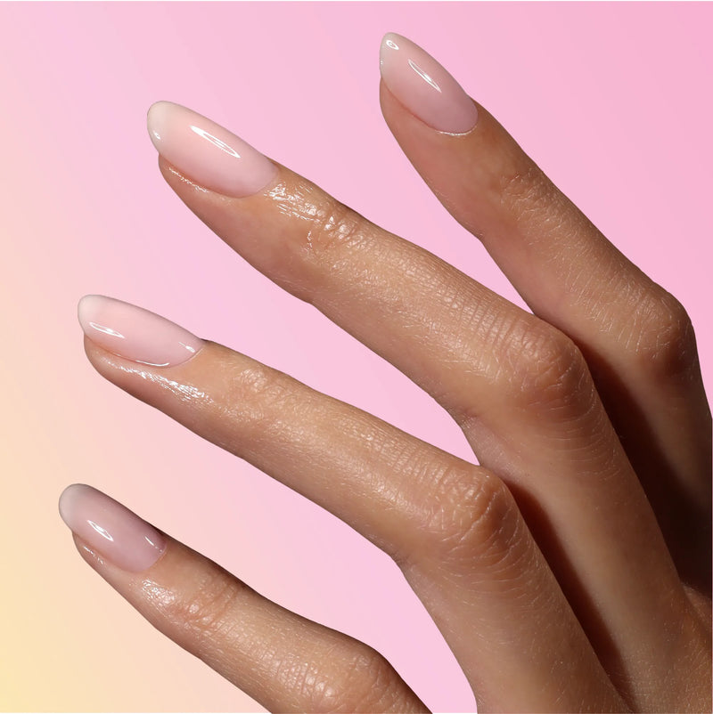 A hand with long, almond-shaped nails painted in LONDONTOWN's BFF sheer pink polish against a pink and yellow gradient background.