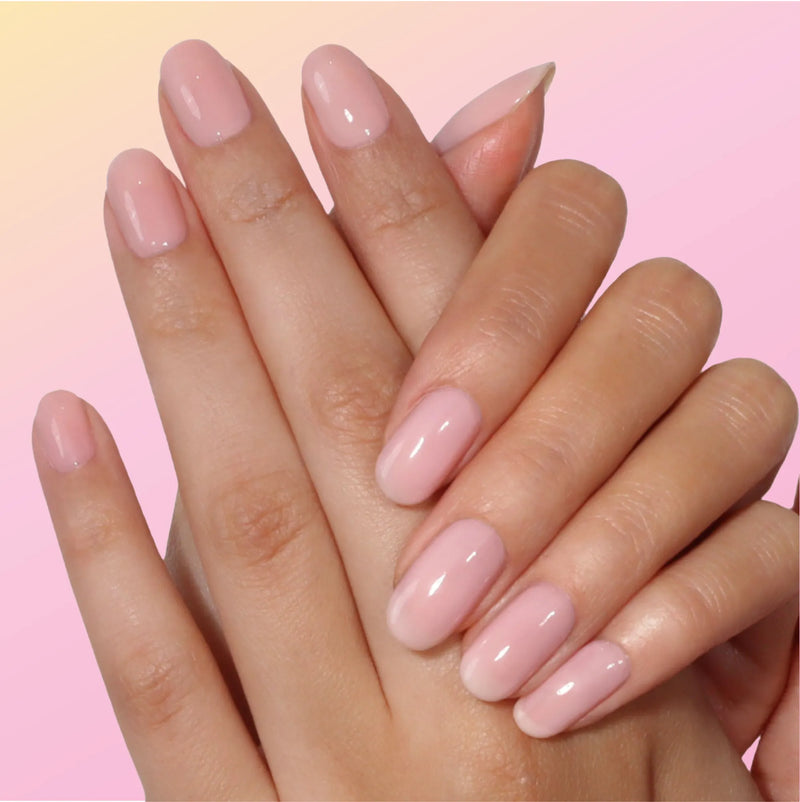 Hands with neatly manicured, oval nails polished in the warm pink "BFF" shade by LONDONTOWN, set against a pink gradient background.
