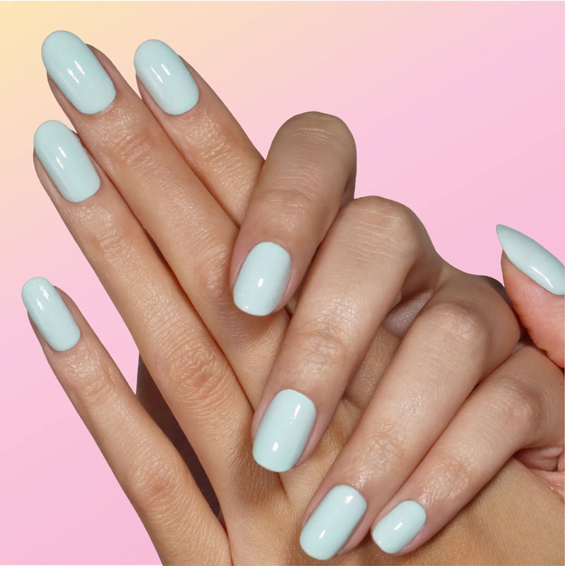 Two hands with neatly manicured nails coated in LONDONTOWN’s Beary Minty, a glossy light blue, exude airy clarity against a vibrant pink and yellow gradient background.