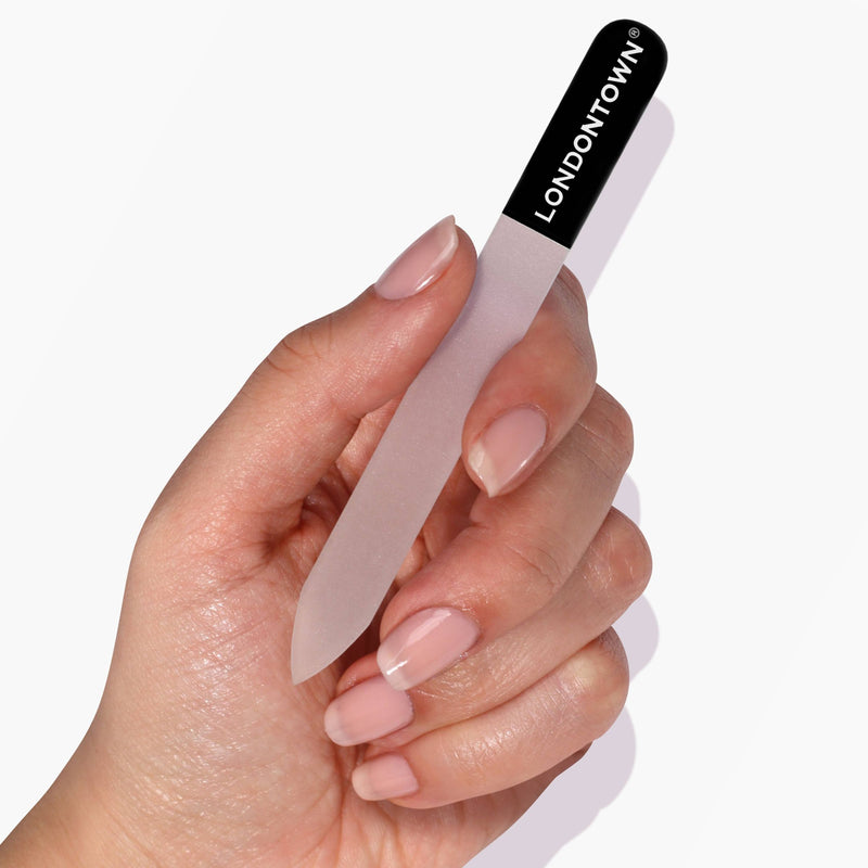 A hand holding the LONDONTOWN Glass Nail File - Black against a white background, promising effortless and damage-free nail filing.