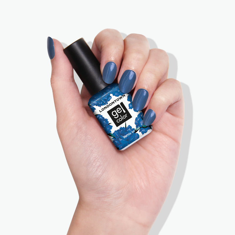 A hand with sporty blue painted nails holds a LONDONTOWN Blue Diamond gel color nail polish bottle adorned with a chic blue and black floral design.