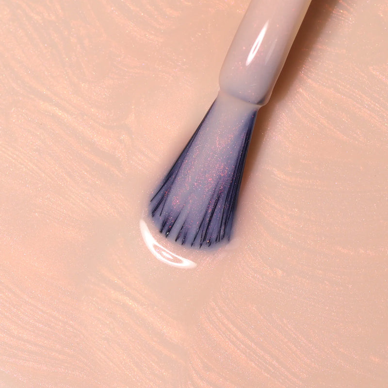 A close-up of a LONDONTOWN Bubble Illuminating Nail Concealer brush with bubblegum pink polish, resting on a swirled surface of matching color.