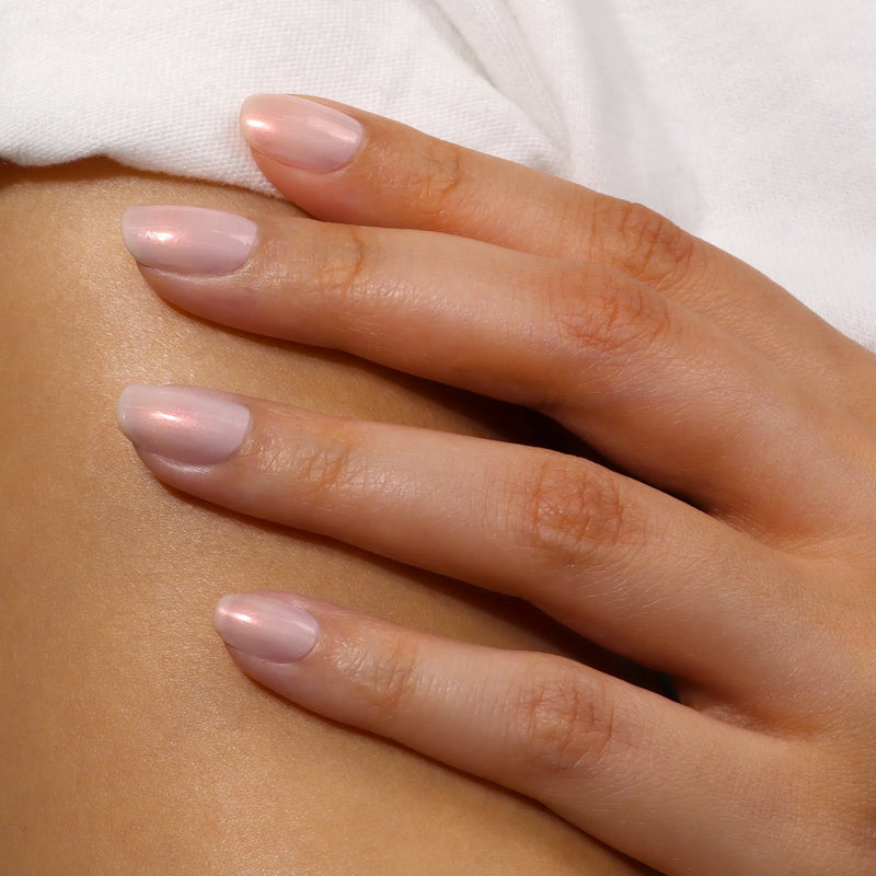 A hand with neatly manicured nails painted in LONDONTOWN's Bubble Illuminating Nail Concealer rests against bare skin, highlighting a glossy, flawless finish.