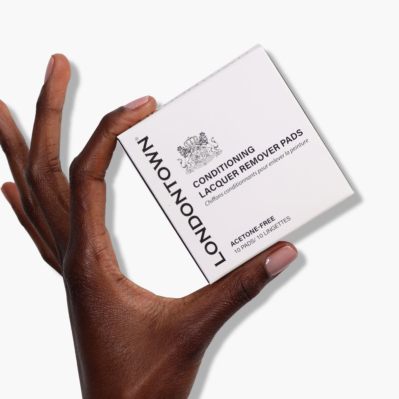 A hand holds a box of LONDONTOWN Conditioning Lacquer Remover Pads against a white background, ideal for convenient nail polish removal on-the-go.