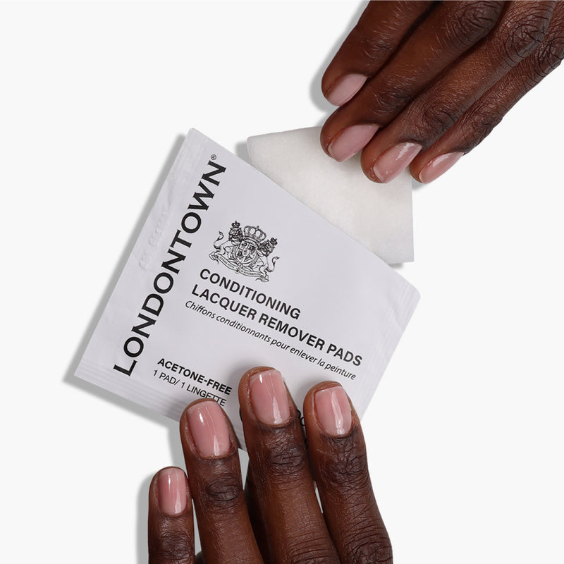 Hands opening a LONDONTOWN Conditioning Lacquer Remover Pads packet, ideal for convenient nail care, with a pad partially visible.
