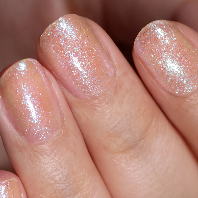 Close-up of fingers with short, neatly manicured nails painted in LONDONTOWN’s Chasing Rainbows, a sheer peach polish with fine iridescent shimmer that catches the light softly.