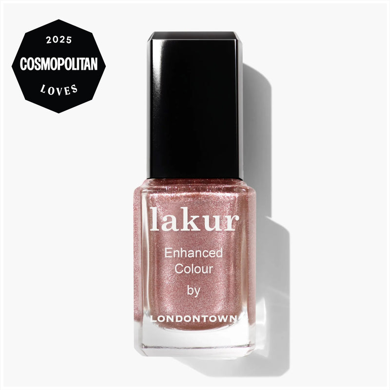 A bottle of LONDONTOWN Lakur Enhanced Colour nail polish in "Extra Bubbles, Please," featuring a sheer mauve hue with shimmering mauve accents and a black cap, shown with a "2025 Cosmopolitan Loves" badge in the top left corner.