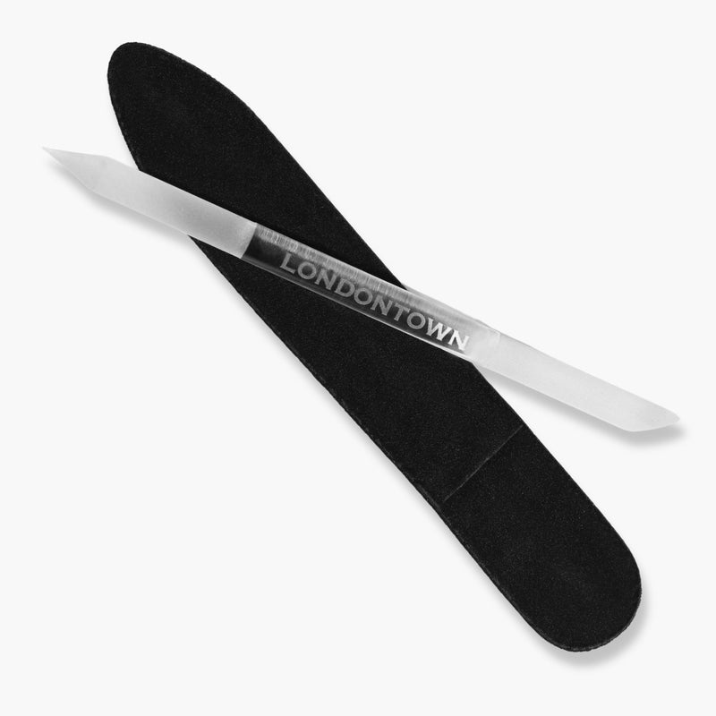 The LONDONTOWN Glass Cuticle Pusher rests diagonally on a black velvet sleeve against a white background, serving as an elegant tool for refining manicures.