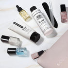 A flat lay of the LONDONTOWN Discovery Set 2.0 displays nail care essentials—polishes, lotion, cuticle oil, a nail file, and a beige zippered pouch—arranged on a light surface.
