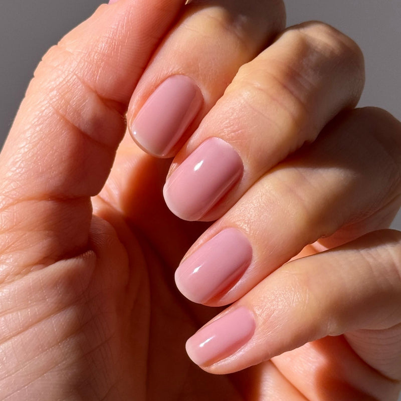 A hand with short, neatly manicured nails painted in LONDONTOWN’s Dream State, a glossy light pink iridescent cream that catches the light with a soft glow.