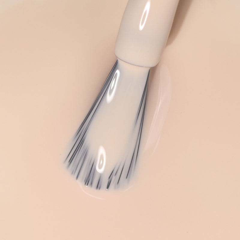 A nail polish brush is immersed in LONDONTOWN's light neutral peach nail polish, Dusk.