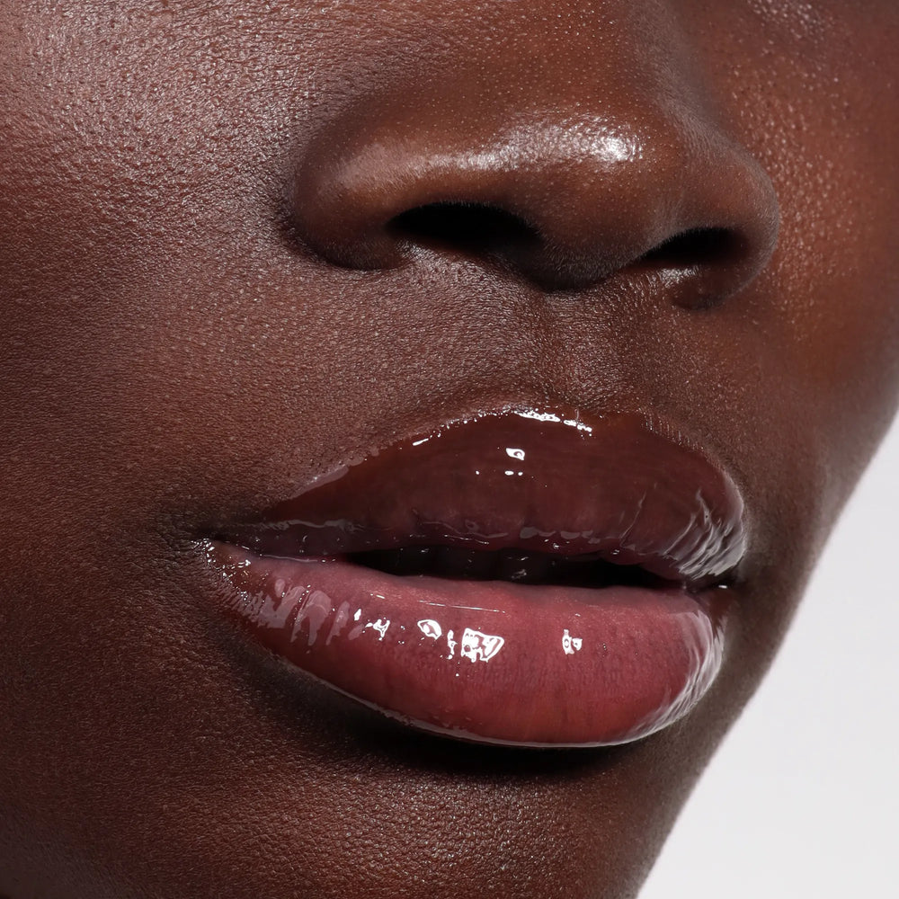 Close-up of smooth dark skin and glossy, naturally pink lips enhanced by LONDONTOWN's Quench Glow Buttery Lip Oil in Flushed.