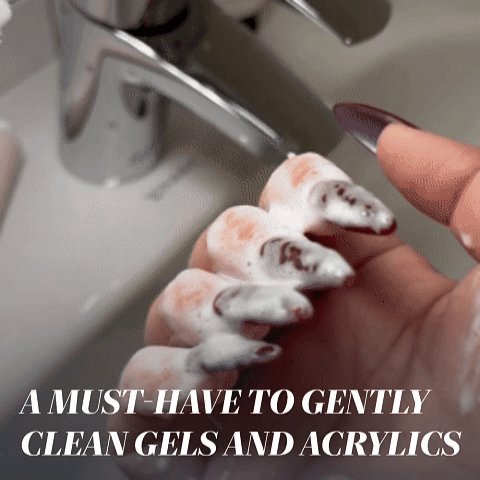 A hand with long acrylic nails is gently washed with soap as text reads: "LONDONTOWN Mani Bright Nail Scrub—essential for cleaning gels, acrylics, and stained nails.