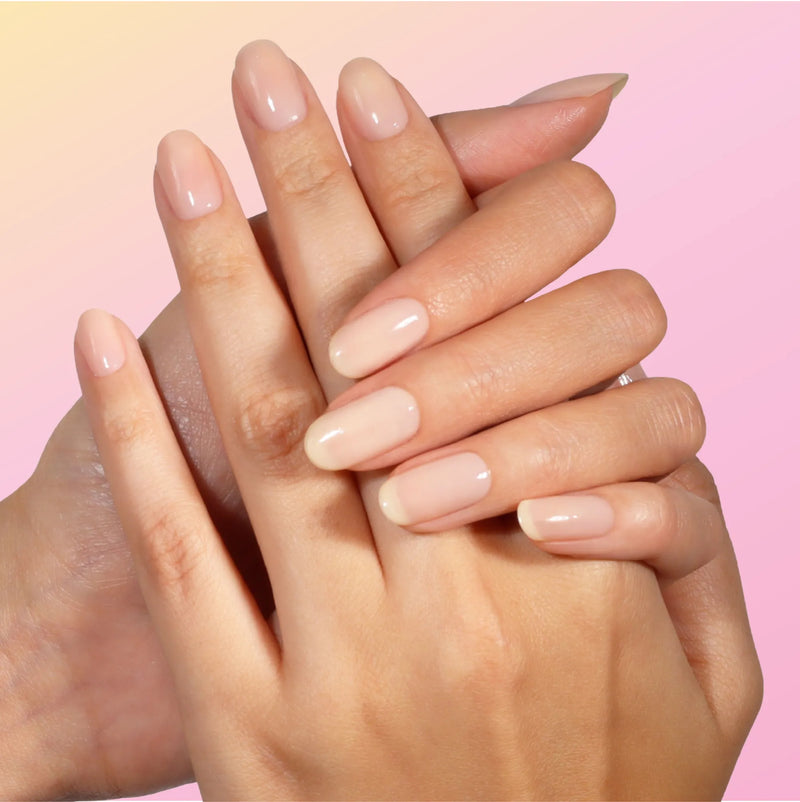 Close-up of two hands with neatly manicured nails painted in LONDONTOWN's Good Vibes Only, a nude shade, against a soft pink gradient background.