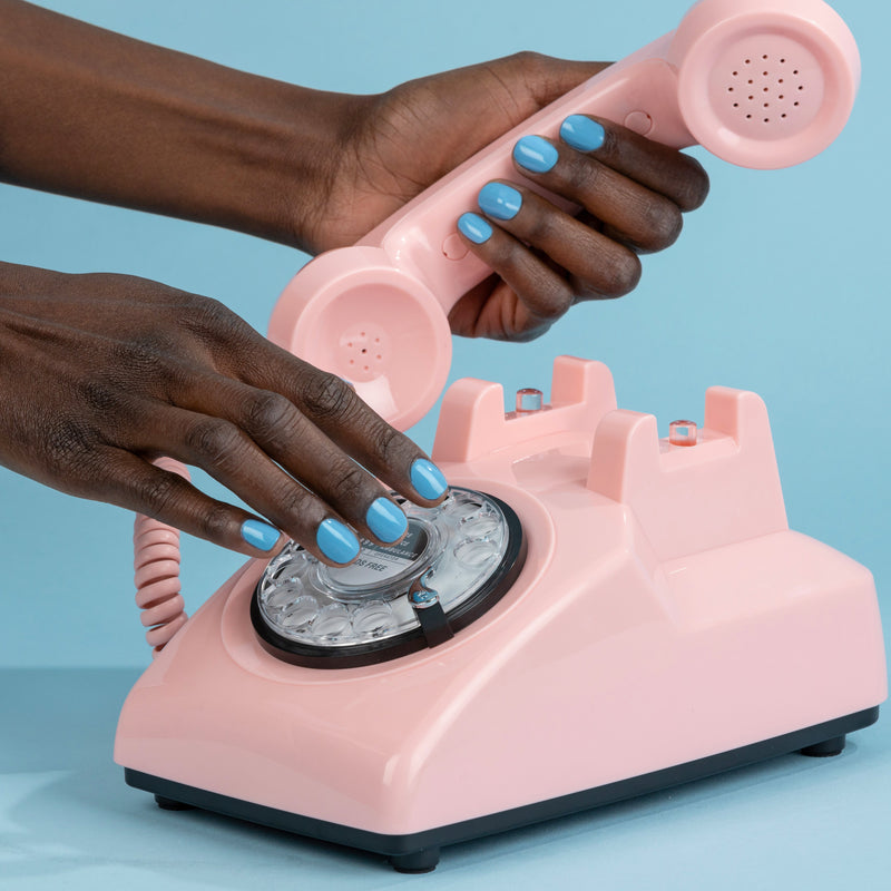 A person with Hot Spring nail polish from LONDONTOWN is dialing a pink rotary phone and holding the receiver.