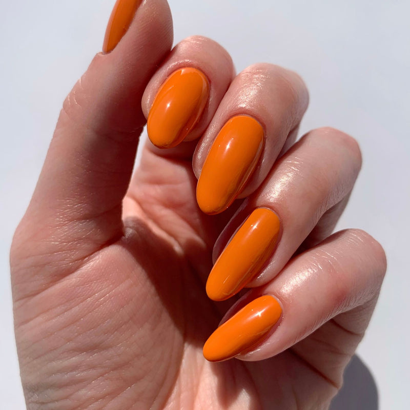 Close-up of a hand with long, almond-shaped nails painted in the striking burnt orange "Heat Wave" nail polish by LONDONTOWN.