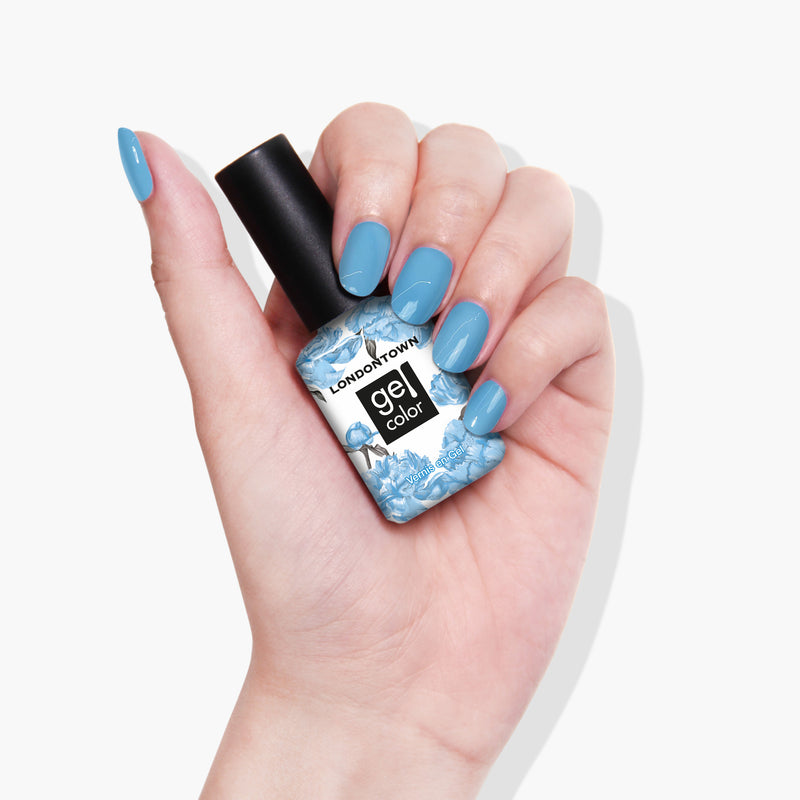 A hand with blue-painted nails holds a bottle of LONDONTOWN Hot Spring Gel Color nail polish, its vibrant hue reminiscent of the crystal-clear Pacific waters.