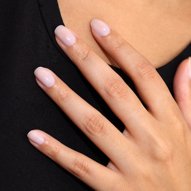 Close-up of a hand with neatly manicured nails, enhanced by LONDONTOWN's Illuminating Nail Concealer to showcase a soft, pale pink color, resting on black fabric.